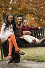 African American mother and children sitting on park bench