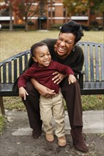 African American mother and son playing on park bench