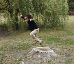 African American boy playing on stump in park