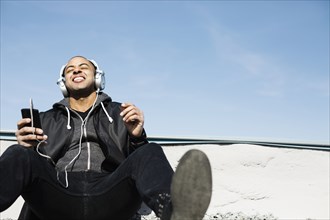 Mixed race man listening to headphones on beach