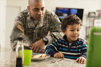 Mixed race soldier father and son eating in kitchen