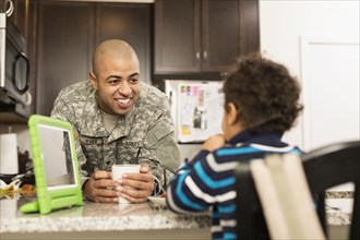 Mixed race soldier father and son eating in kitchen