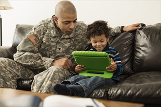 Mixed race soldier father and son using digital tablet on sofa