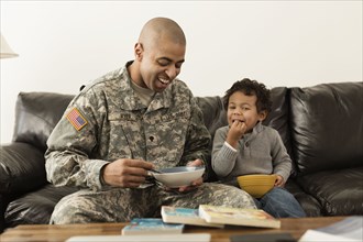 Mixed race soldier father and son from bowls on sofa