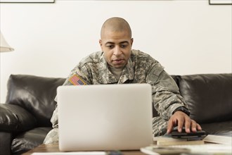 Mixed race soldier using laptop on living room sofa