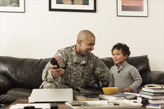 Mixed race soldier father and son watching television in living room