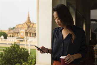 Asian businesswoman using cell phone at window