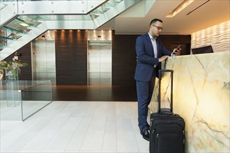 Hispanic businessman using cell phone at hotel front desk