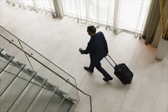 High angle view of Hispanic businessman rolling luggage in hotel lobby