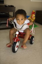 Mixed race boy riding tricycle in living room