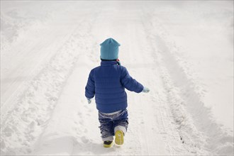 Caucasian boy walking in tire tracks in snow