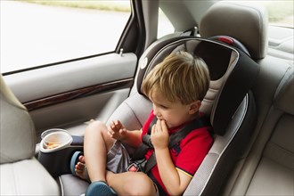 Caucasian boy eating snack in car seat