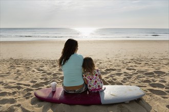 Mother and daughter sitting on surfboard at beach