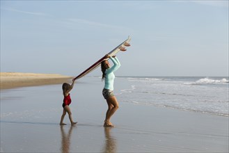 Mother and daughter carrying surfboard on beach