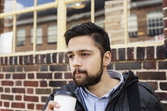 Hispanic man carrying bag drinking coffee in city