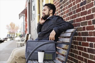 Hispanic man sitting on city bench using cell phone