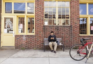 Hispanic man sitting on city bench using cell phone