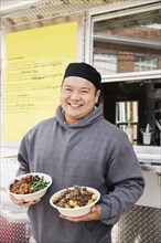 Asian man holding bowls of food at food truck