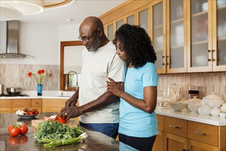 Black couple chopping vegetables in kitchen