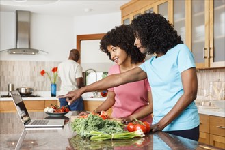 Black women using digital tablet and chopping vegetables in kitchen
