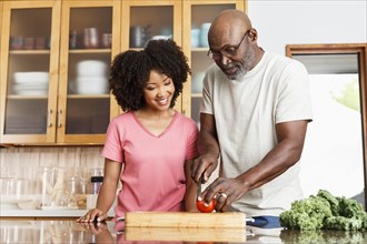Black father and daughter chopping tomato in kitchen