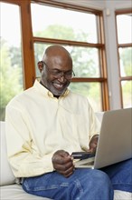 Black man online shopping with credit card and laptop on sofa