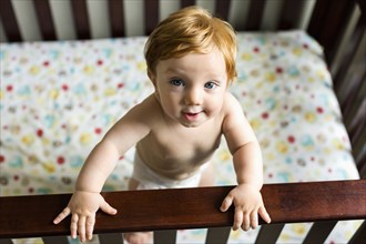 Portrait of curious Caucasian baby boy standing in crib