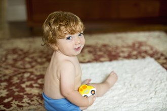 Caucasian baby boy sitting on rug holding toy car