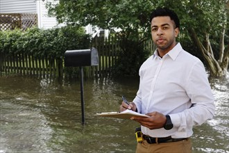 Black insurance adjuster examining flooding damage to house