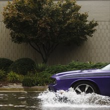 Purple car splashing through water in flood