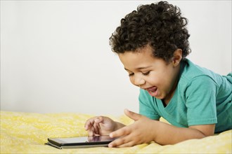 Excited Mixed Race boy laying on bed using digital tablet