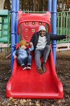 Father and son on playground slide in park