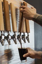 Hands of Caucasian man pouring beer from tap