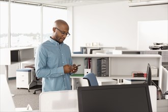 African American man texting on cell phone in office