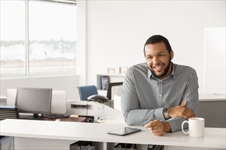 Smiling Mixed Race man leaning in office