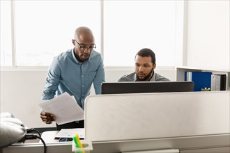 Men working at computer with paperwork in office