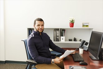 Mixed Race man reading paperwork near computer in office