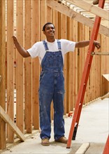 Portrait of smiling mixed race man leaning on ladder at construction site