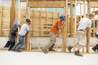 Volunteers pushing framed wall at construction site