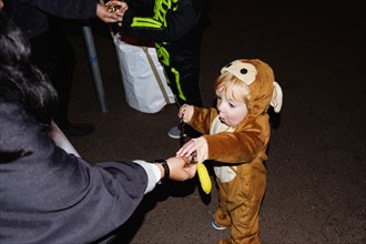 Woman giving treats to Caucasian boy wearing a bear costume