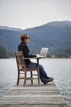 Caucasian woman using laptop on wooden dock on lake