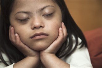 Mixed race Down syndrome girl resting with chin in hands
