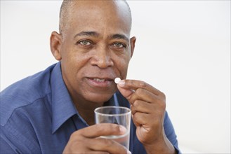 Senior African man taking medication with glass of water