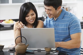 Asian couple using laptop with credit card in kitchen