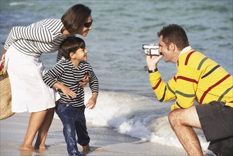 Indian father video recording wife and son at beach
