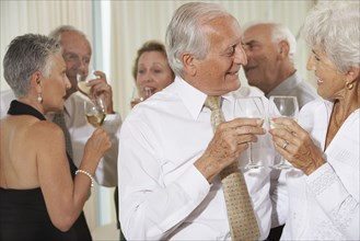 Senior couple toasting at party with friends in background