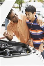 Middle Eastern father and son looking under car hood