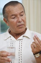 Hispanic man taking pill with water