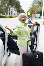 Senior African American woman standing with car and luggage