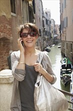 Smiling Italian woman talking on cell phone near canal